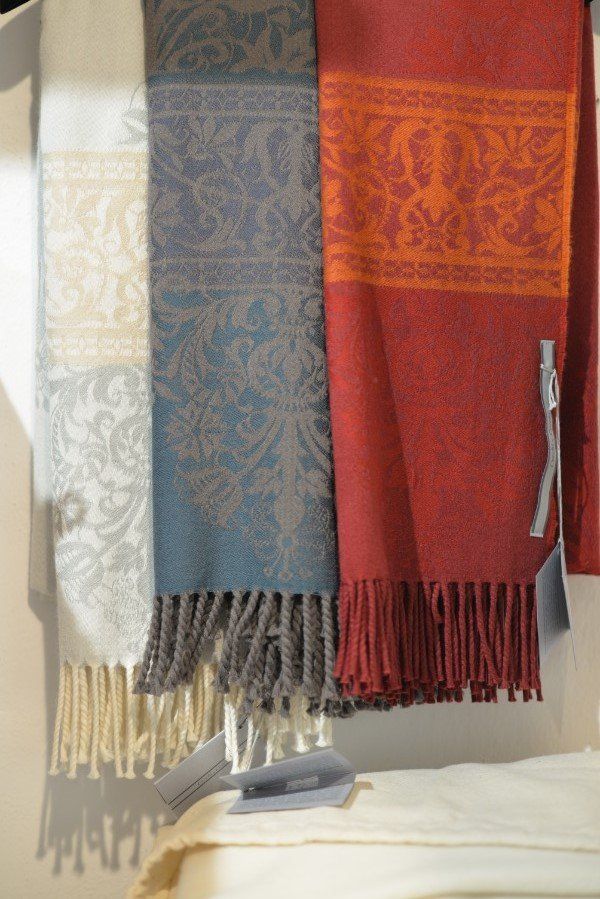 Sciarpe tessute appese, nei colori crema, blu e rosso con frange, esposte su un appendiabiti.