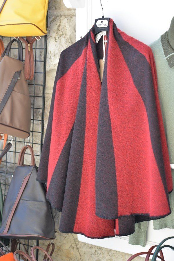 Indumento simile a un mantello, di colore rosso e nero, appeso a una gruccia in un negozio di abbigliamento.
