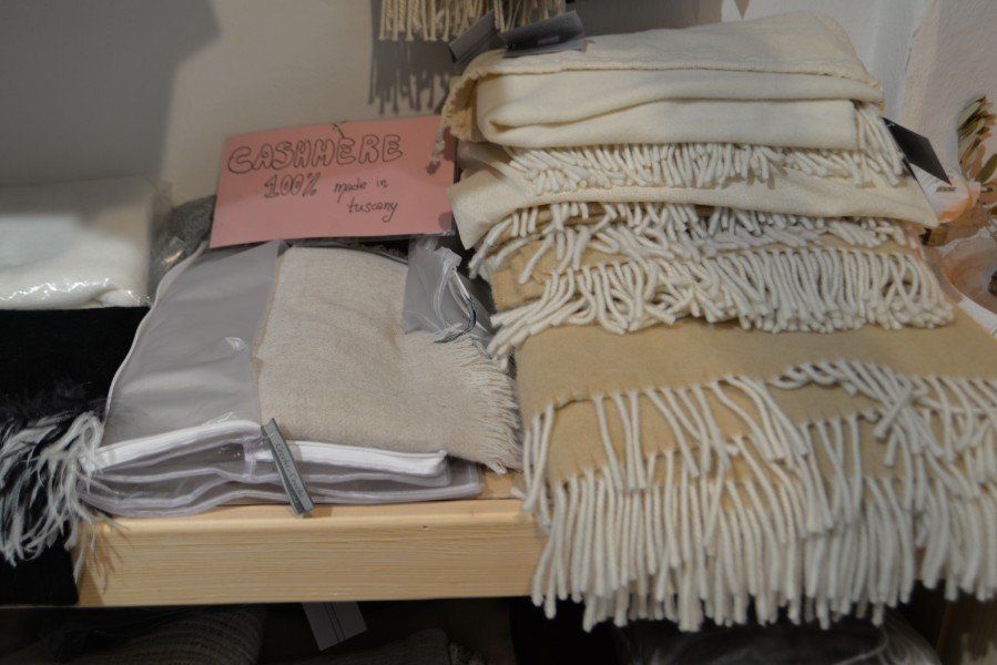Coperte piegate e plaid di lana impilati su uno scaffale, con un cartello rosa con la scritta