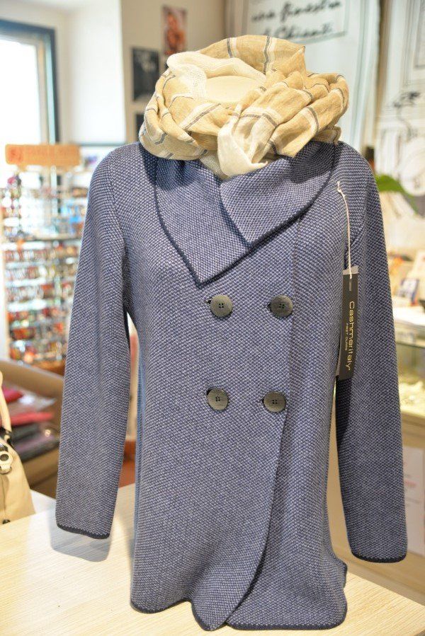 Cappotto blu doppiopetto con ampio colletto a balze color crema, esposto su un manichino in una vetrina di un negozio.