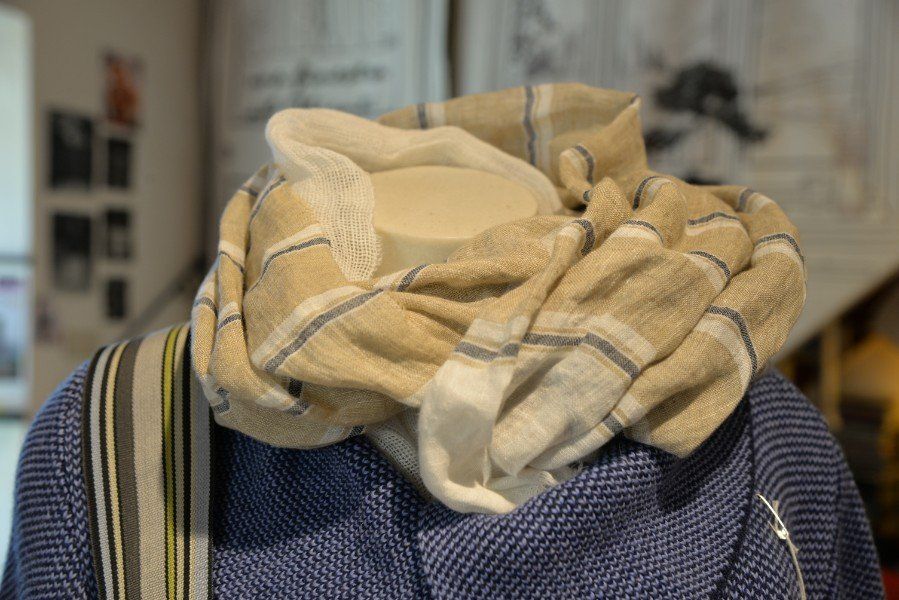 Una sciarpa beige avvolta intorno al collo di un manichino o di una persona, drappeggiata sopra un maglione scuro dalla trama particolare.