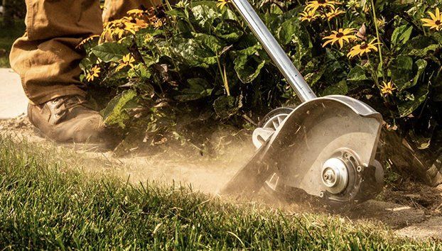 Person edging a lawn, using a trimmer along a sidewalk.