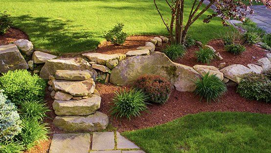 Stone steps and landscaping in a garden with mulch and green plants.