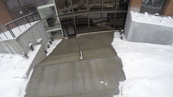Entrance to a building with snow-covered steps and walkway, glass doors.