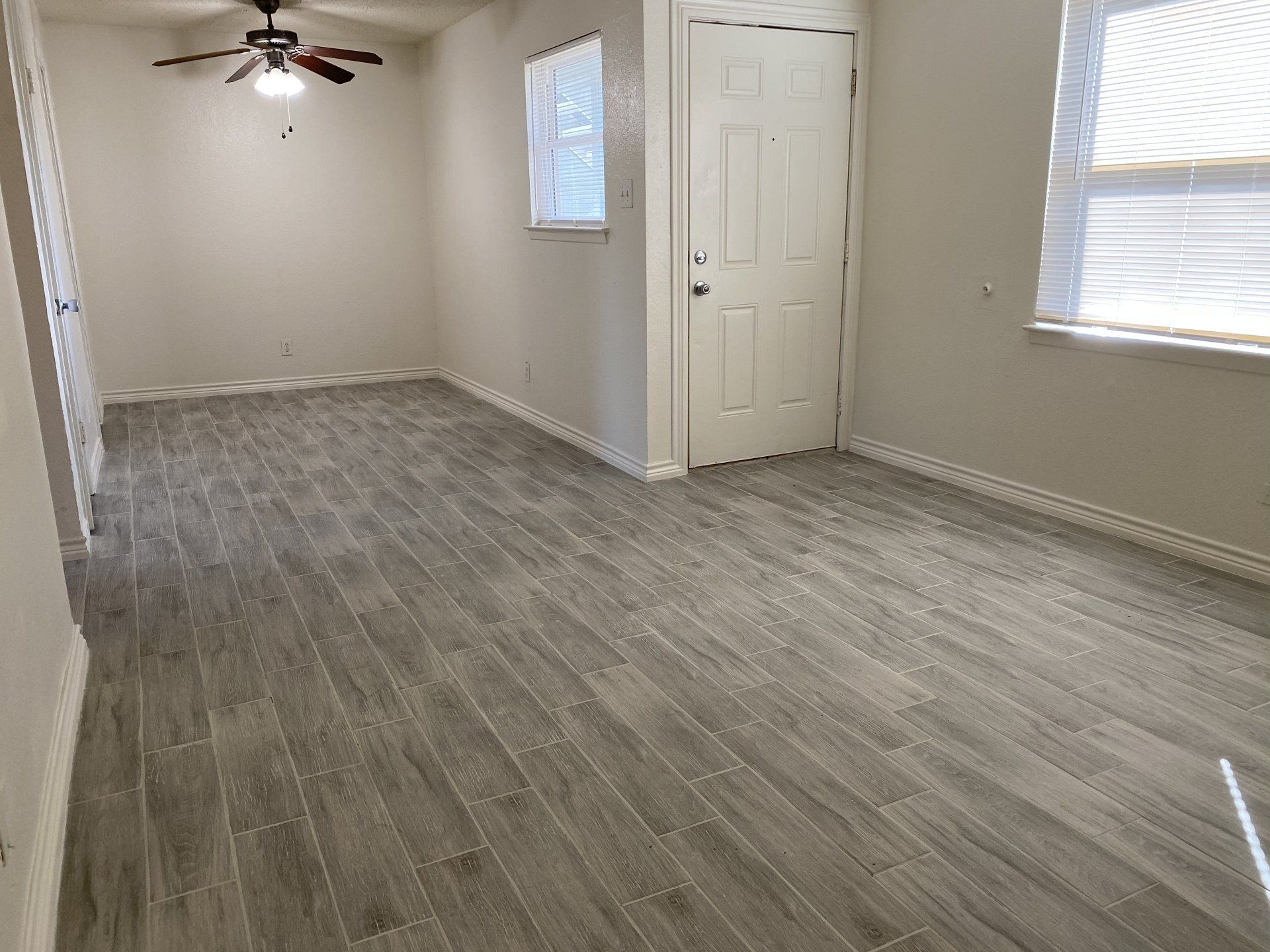Bright 2 bedroom living & dining area with a ceiling fan with light above where the dining table goes, main entry door & 2 large windows 