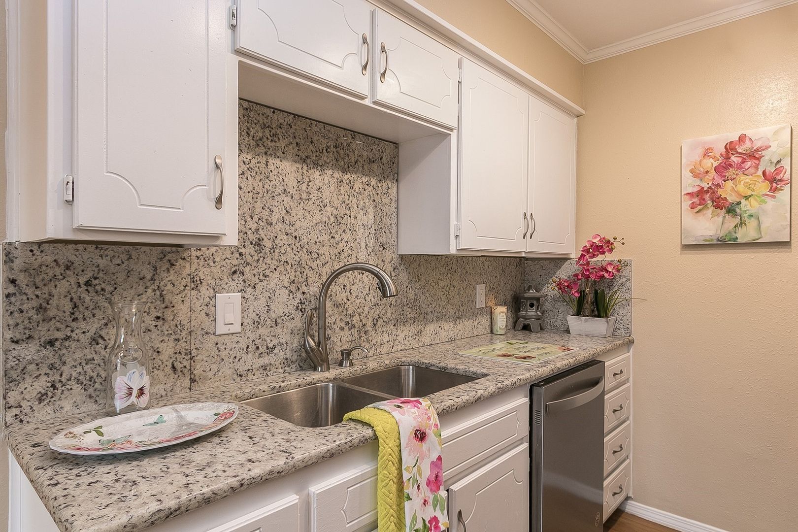 A kitchen with granite counter tops , white cabinets , a sink and a dishwasher.
