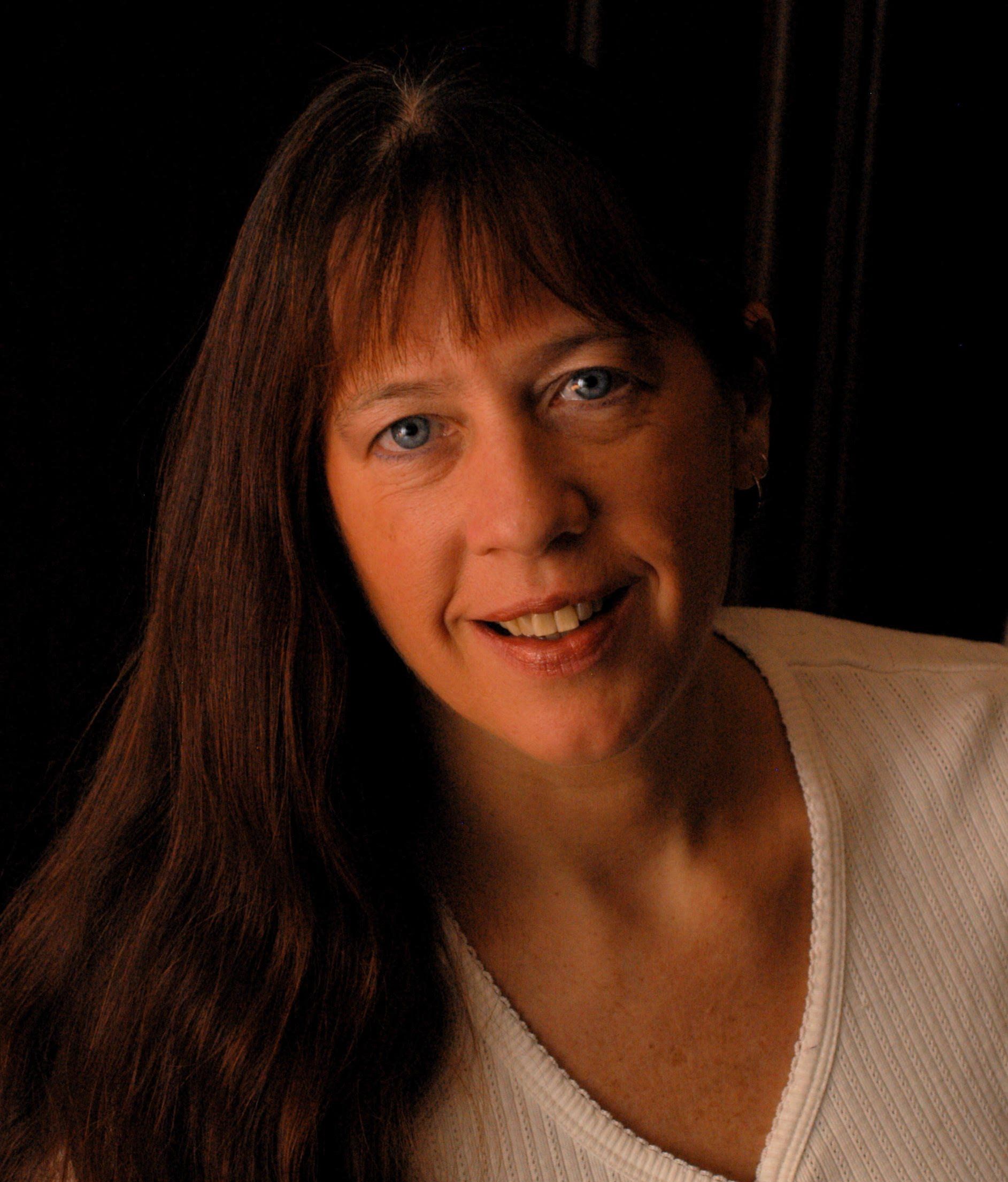 A woman with long brown hair is smiling and wearing a white shirt