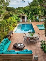 Piscina en el patio trasero con terraza de madera, tumbonas turquesas y una pequeña mesa rodeada de exuberante vegetación.