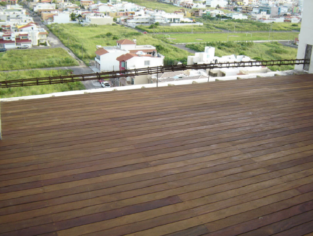 Terraza de madera con vistas a campos verdes y casas en la distancia.