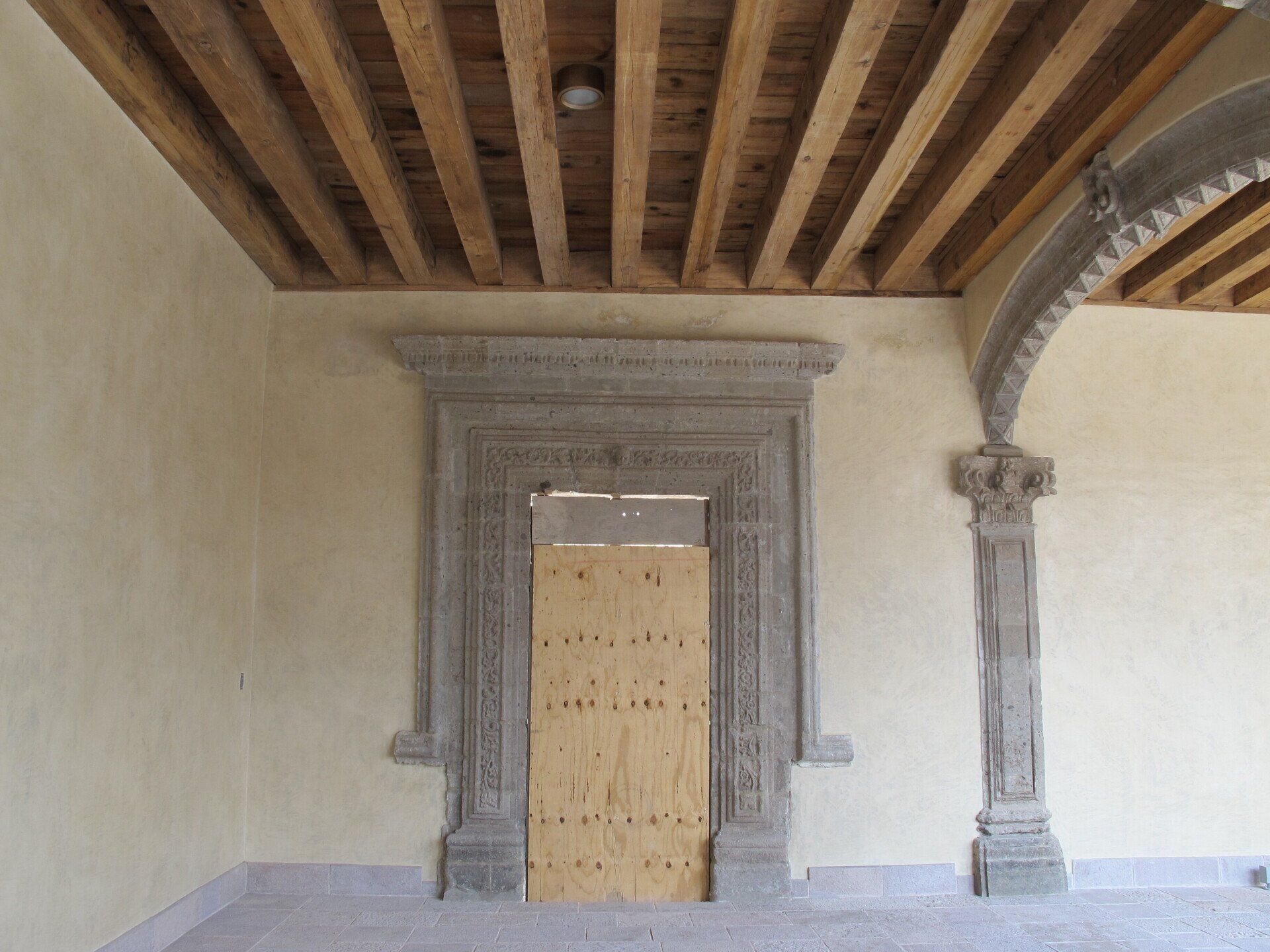 Entrada de piedra con puerta de madera cerrada en una habitación rústica con vigas de madera a la vista en el techo.