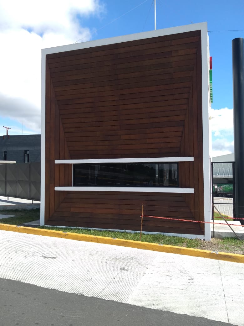 Fachada de edificio moderno con paneles de madera oscura, una ventana horizontal blanca y un cielo azul brillante.