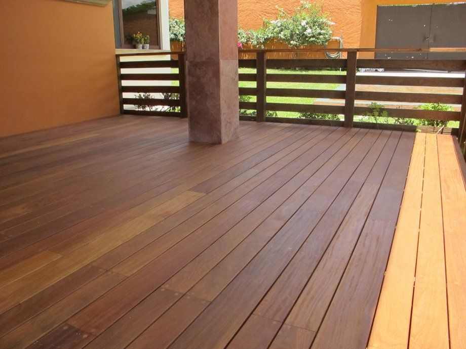 Terraza de madera con barandilla horizontal, paredes naranjas y un jardín con césped más allá.