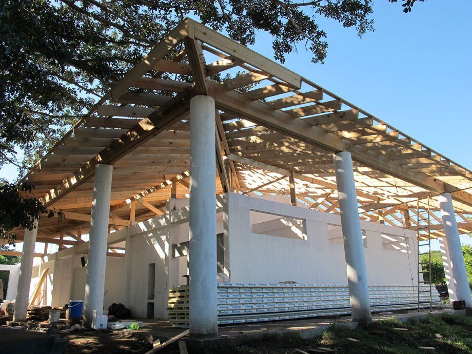 Casa parcialmente construida con cerchas de madera a la vista y columnas blancas en construcción.