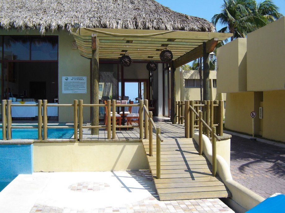Paseo tropical de estilo resort con techo de paja, rampa de madera y asientos junto a la piscina azul.
