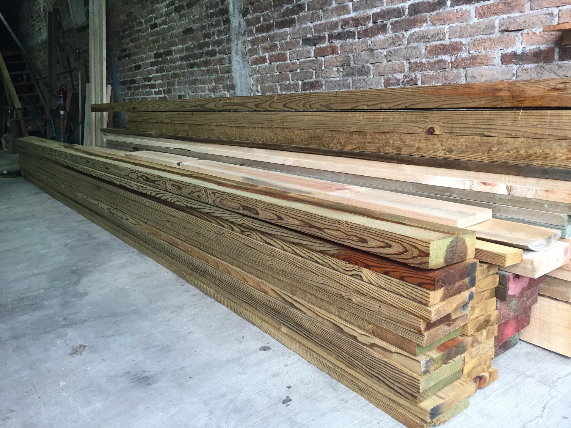 Montones de largas tablas de madera almacenadas en un almacén con paredes de ladrillo.