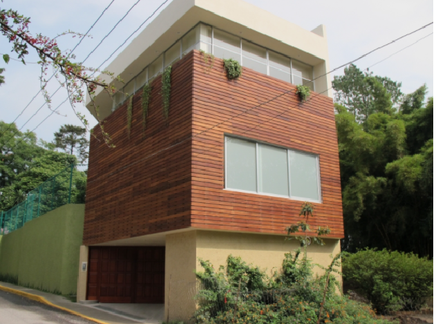 Casa moderna de tres plantas con revestimiento de ladrillo, grandes ventanales y garaje en una ladera arbolada.