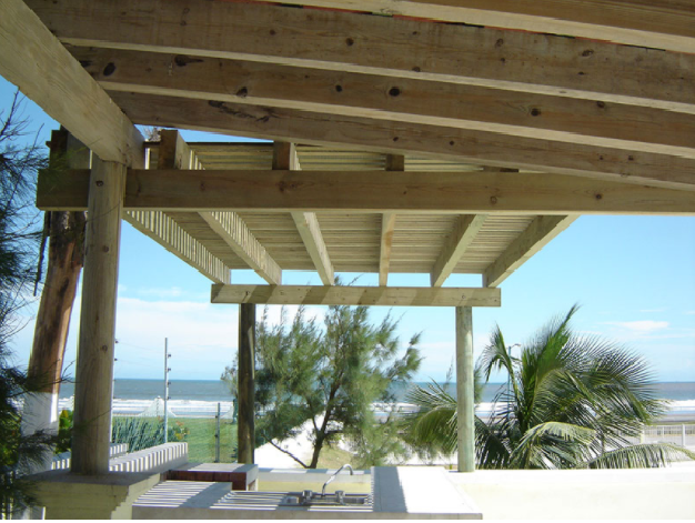 Pabellón de madera en la playa con vistas al océano, con palmeras y tumbonas.
