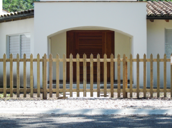 Casa blanca con un porche curvo, contraventanas de madera y una valla de estacas color beige en la parte delantera.