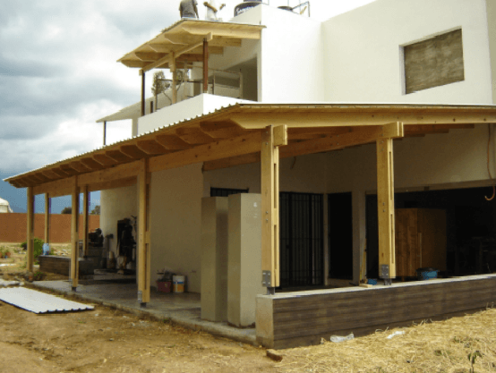 Casa de una sola planta de color beige con porche de madera y tejado inclinado en un entorno rural.