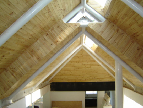 Techo abovedado de madera con vigas a la vista y tragaluces en una habitación interior luminosa.