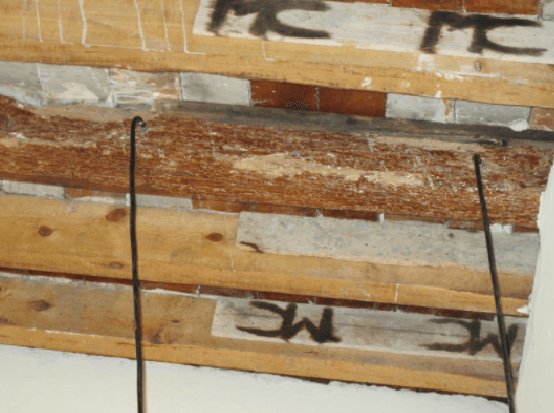 Primer plano de vigas de madera y mampostería con cables negros colgando.