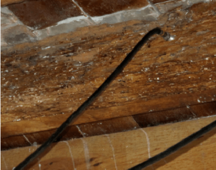 Cable negro extendido sobre toscas tablas de madera cerca de una pared de ladrillos.