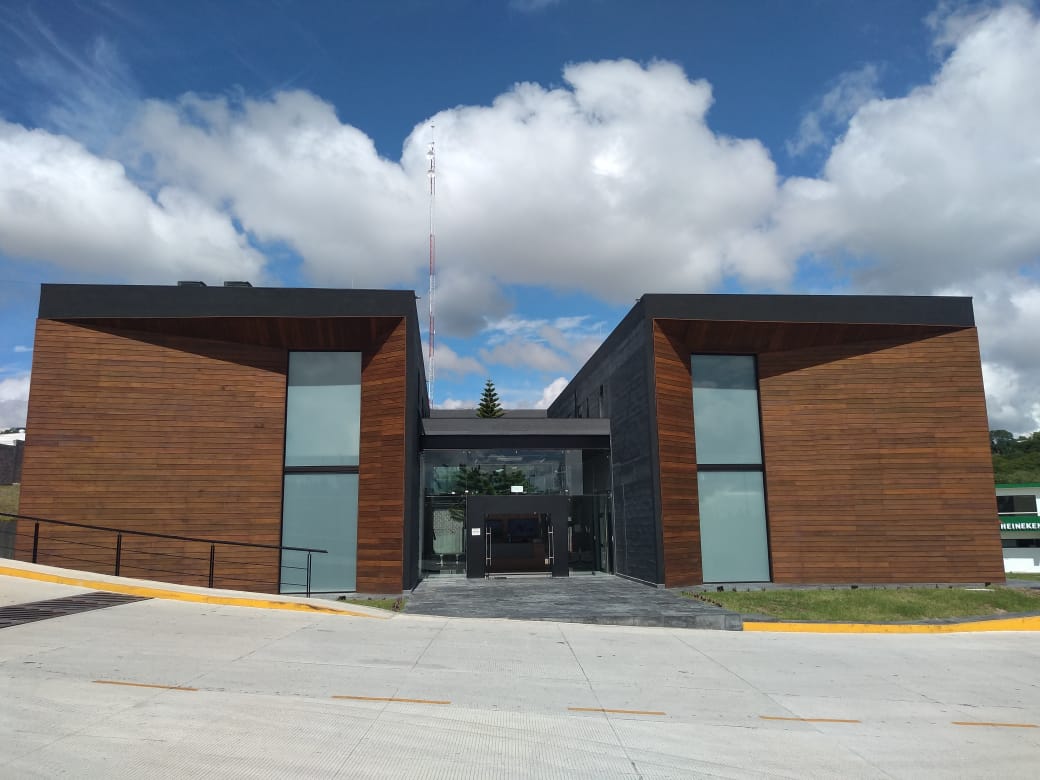Edificio moderno con alas revestidas de madera y una entrada de cristal bajo un cielo nublado.
