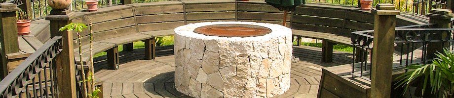 Pasarela de madera alrededor de una hoguera de piedra en un entorno de jardín de parque.
