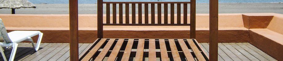 Terraza de madera en la playa con un banco frente al océano y tumbonas a los lados.