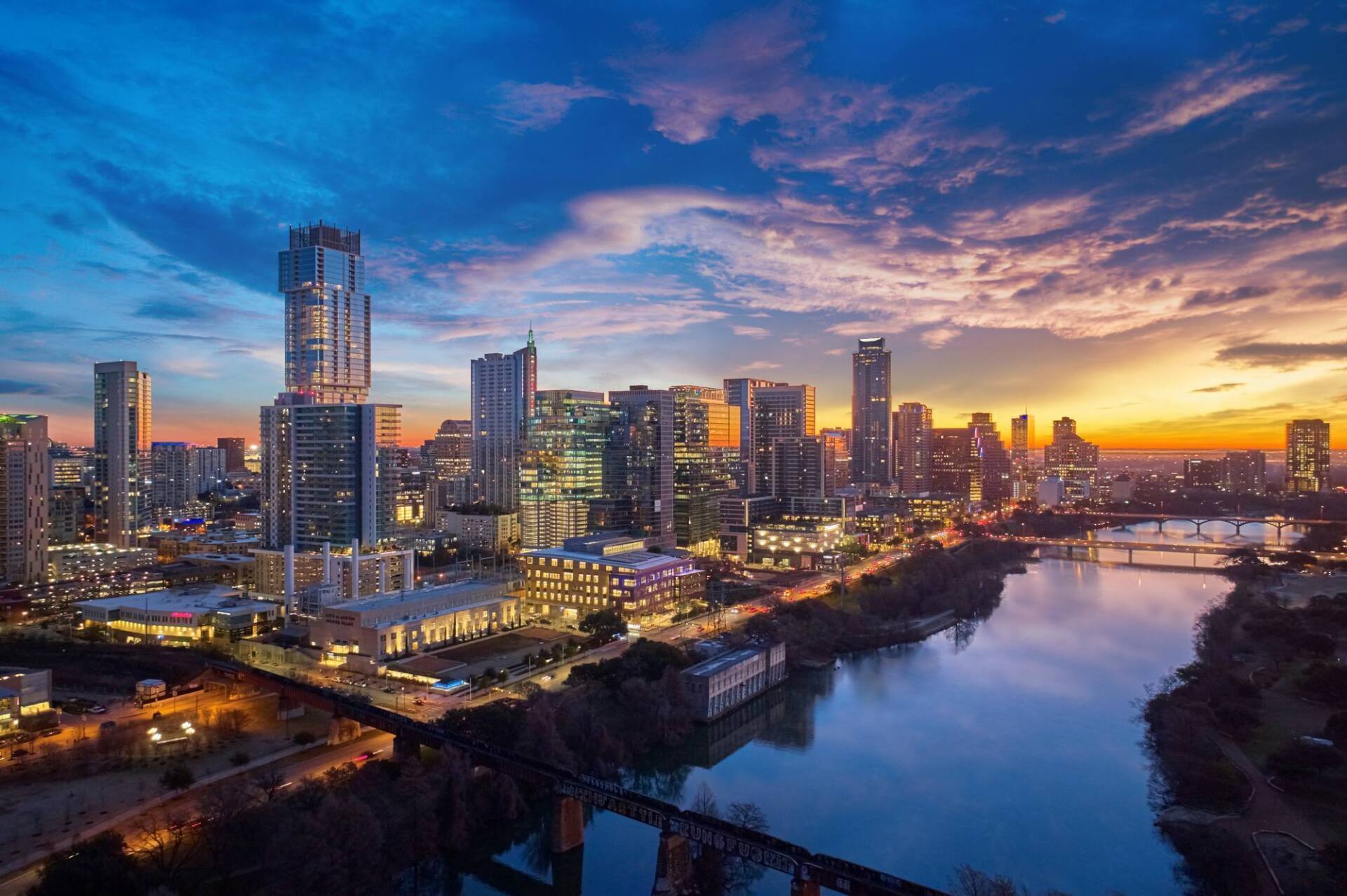 Austin, Texas skyline at sunset with a river in the foreground, buildings, and colorful sky.