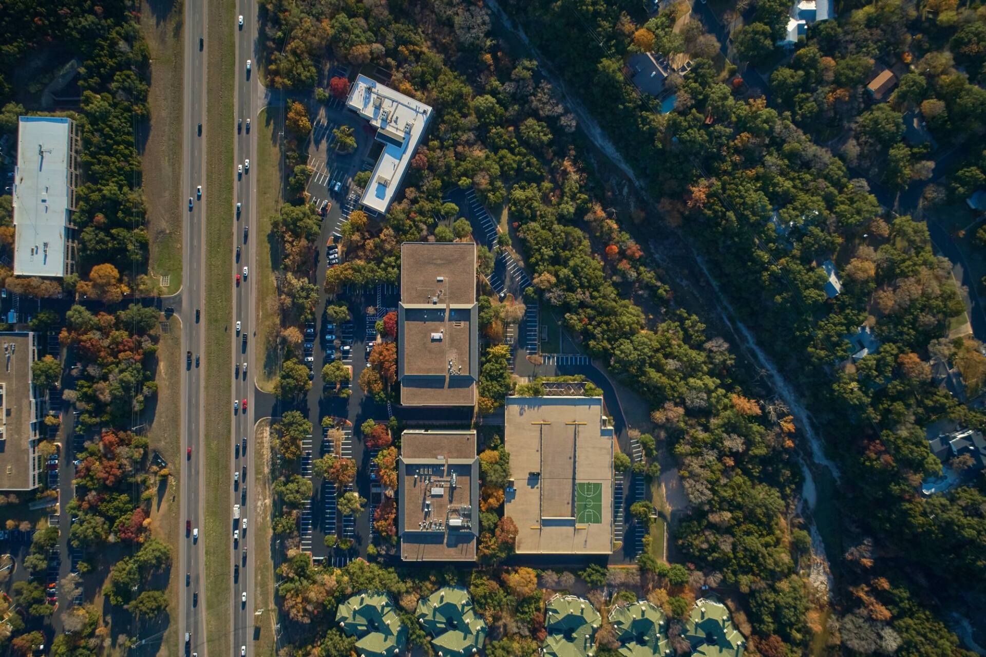Aerial view: Buildings, highway with traffic, and dense trees in fall colors.