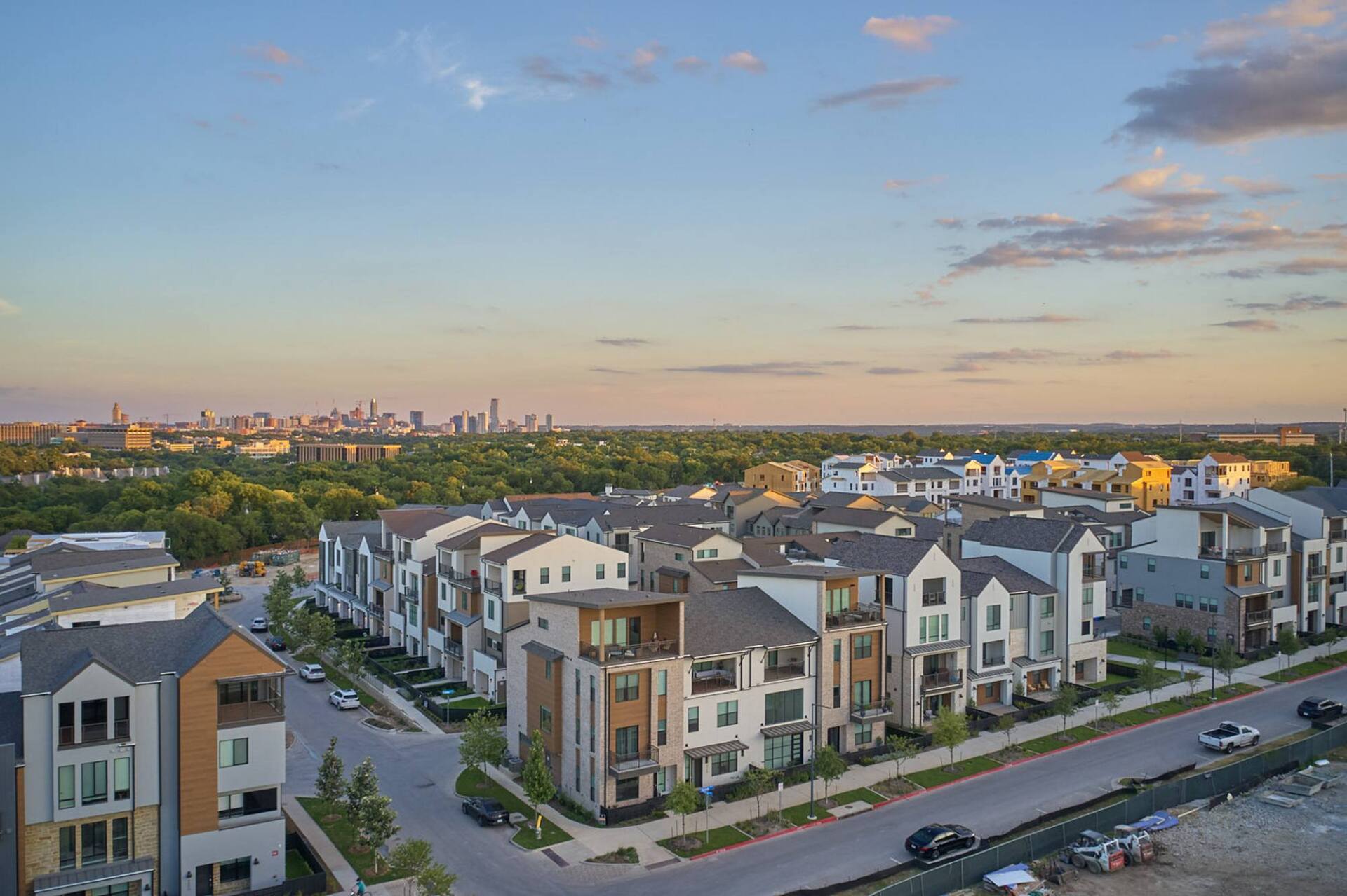 Aerial view of modern townhouses, cityscape in background, under a blue sky.
