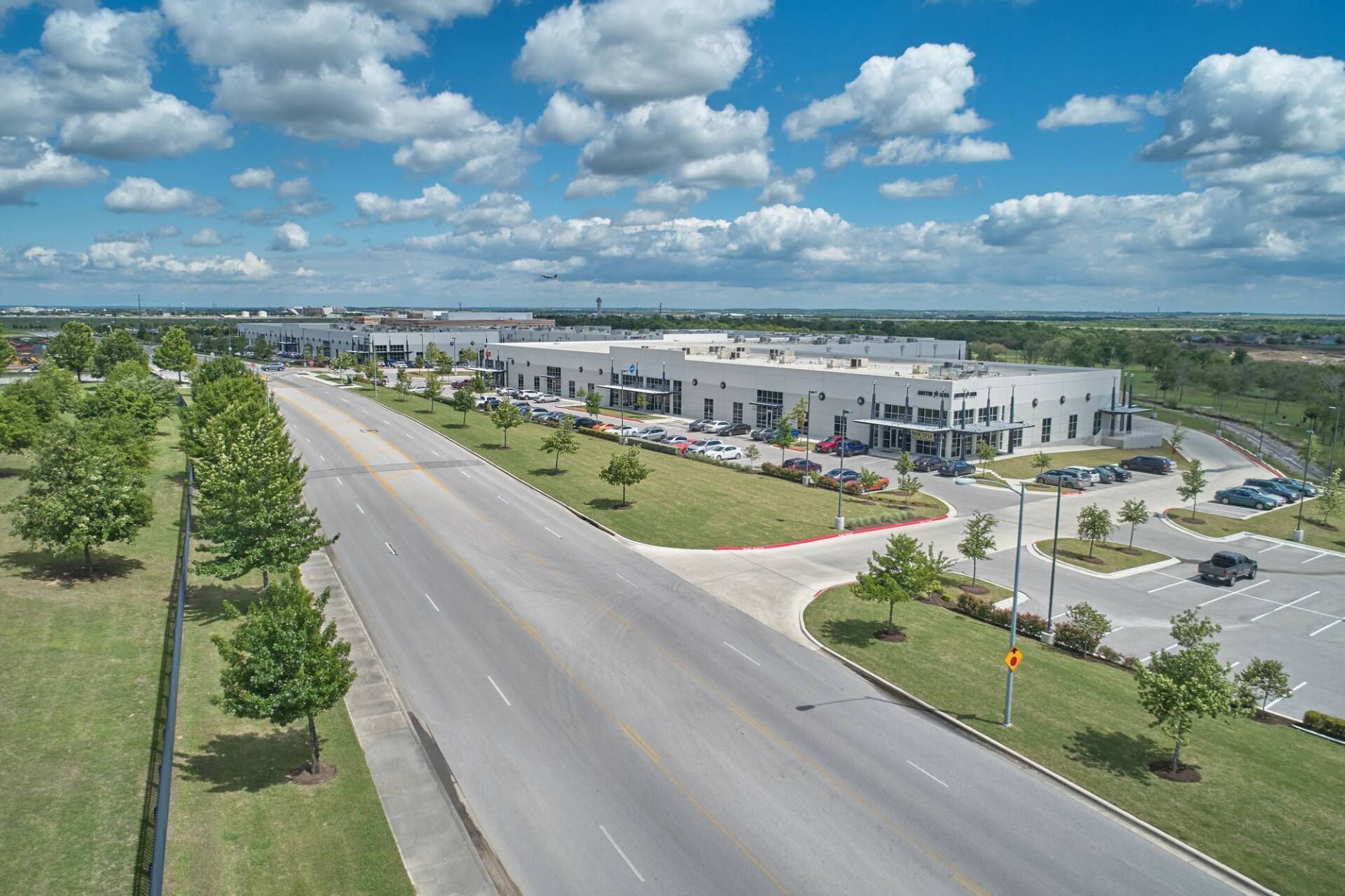 Wide shot of a multi-building industrial complex next to a long, empty road under a partly cloudy sky.
