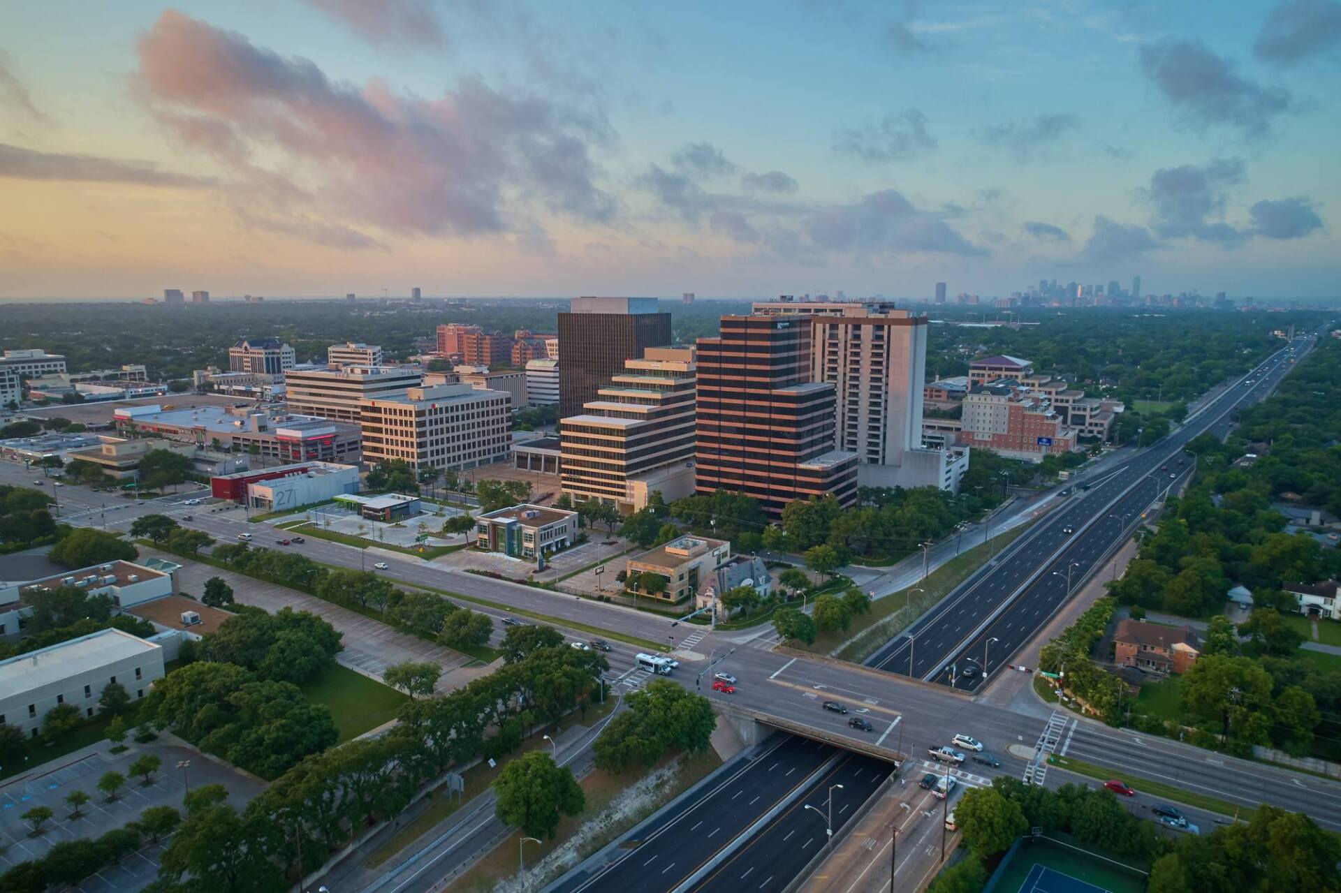 Aerial view of a city with buildings, roads, and a cloudy sky at sunset.