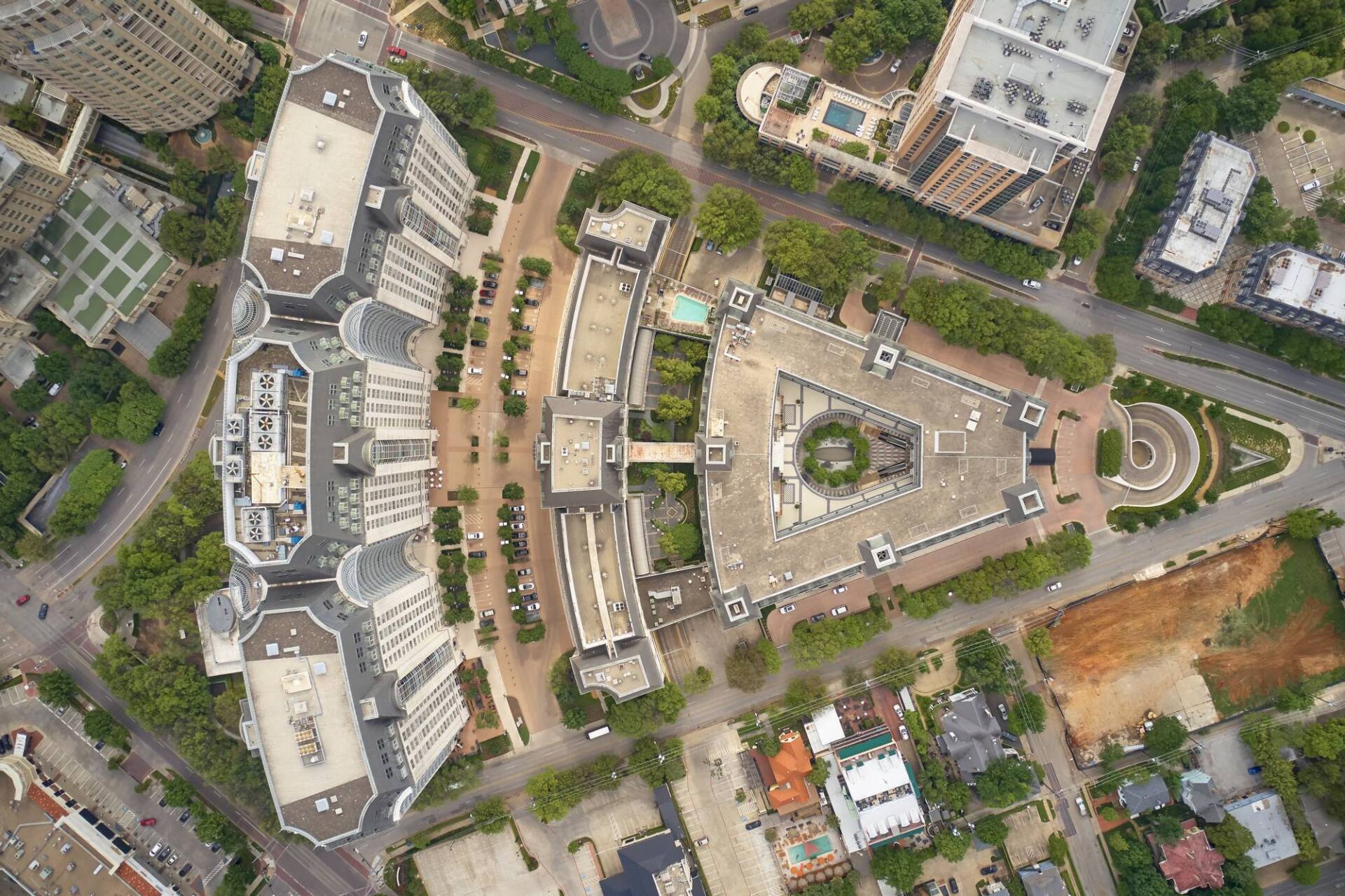 Aerial view of buildings, streets, and trees in an urban setting. Buildings have white facades and gray roofs.