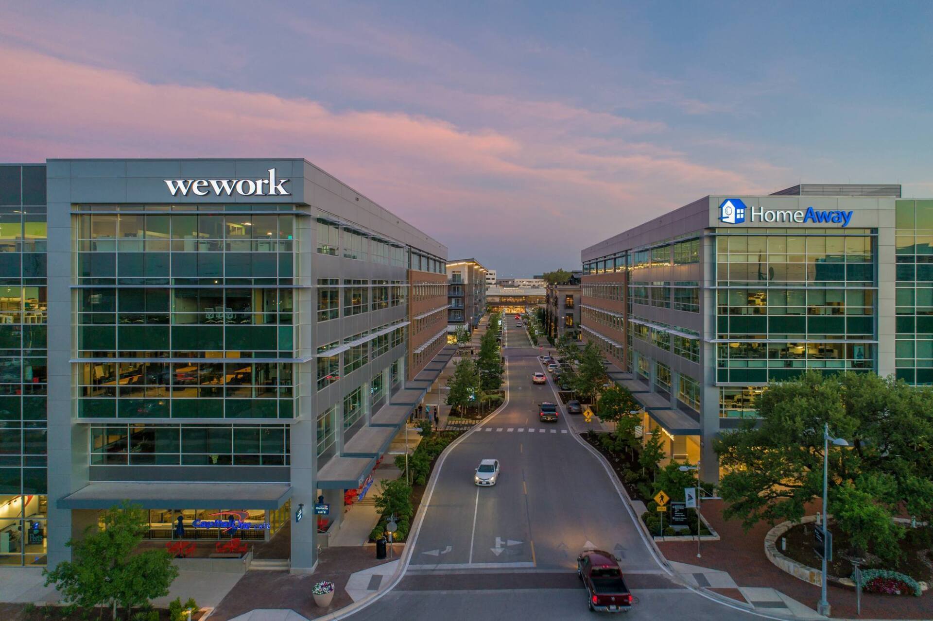 Buildings with WeWork and Humana logos flank a street, under a pink and blue sky at dusk.