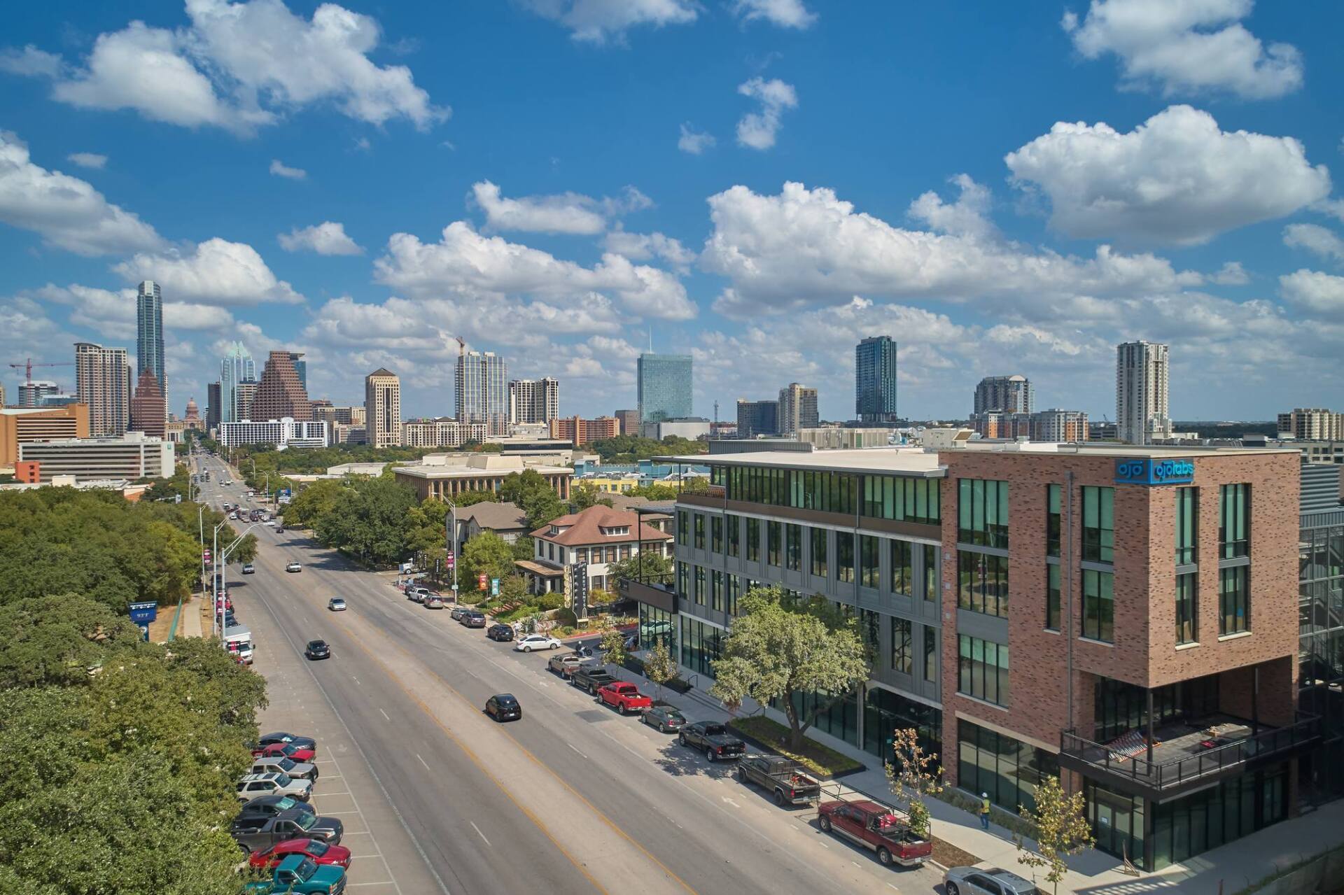 Downtown Austin cityscape with blue sky and fluffy clouds; multi-story buildings and street with cars.