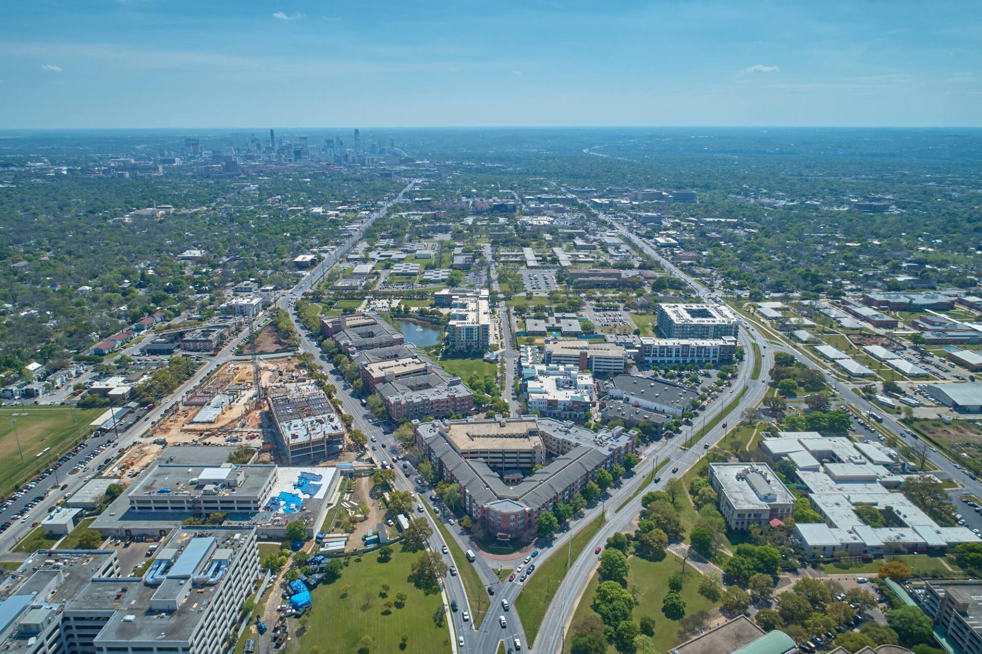 Aerial view of a city with buildings, roads, and green spaces under a clear blue sky.