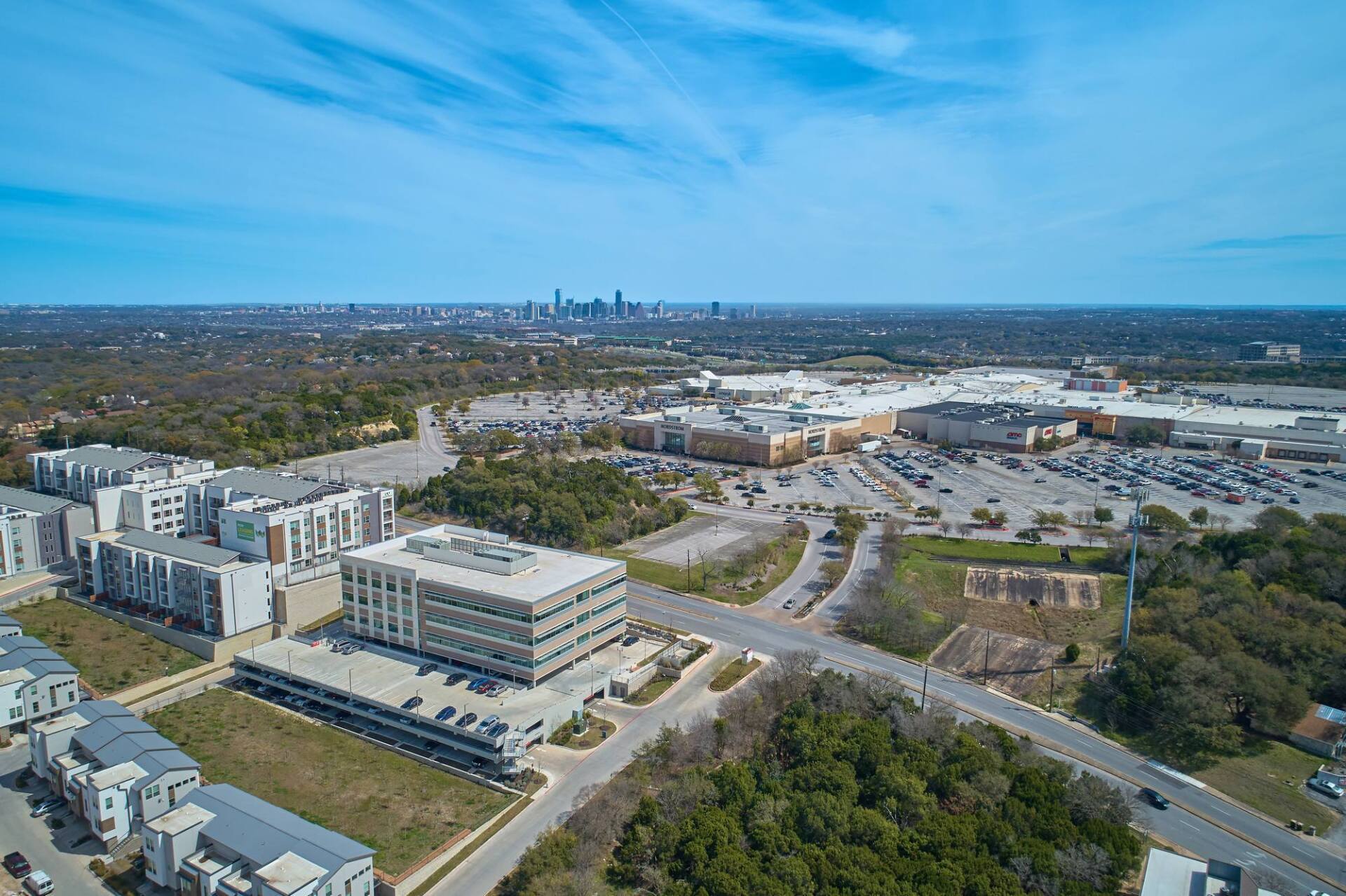 Aerial view of mixed-use development with buildings, parking lots, and shopping center under a blue sky.