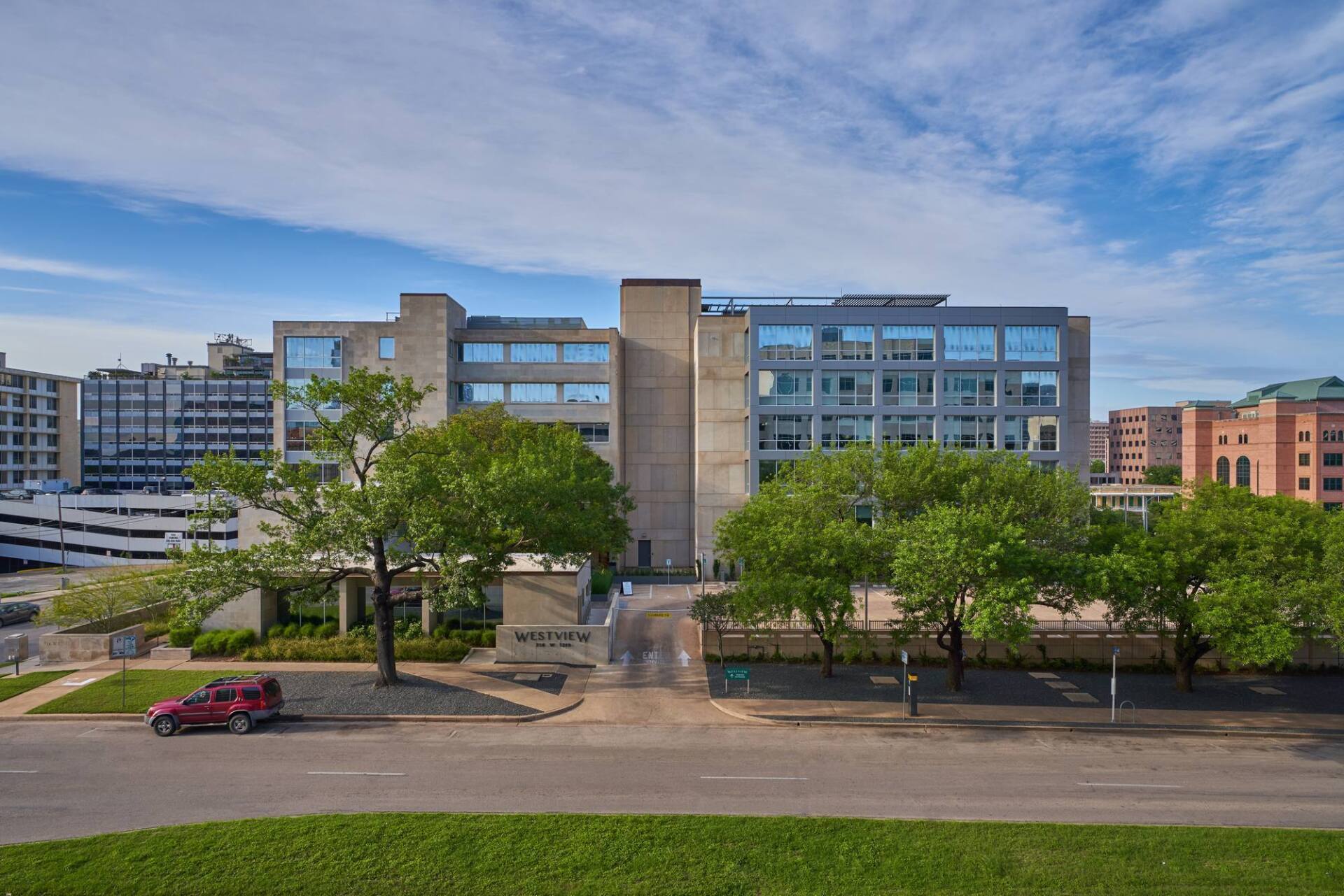 A multi-story building with a light stone facade, trees in front, and a blue sky above.