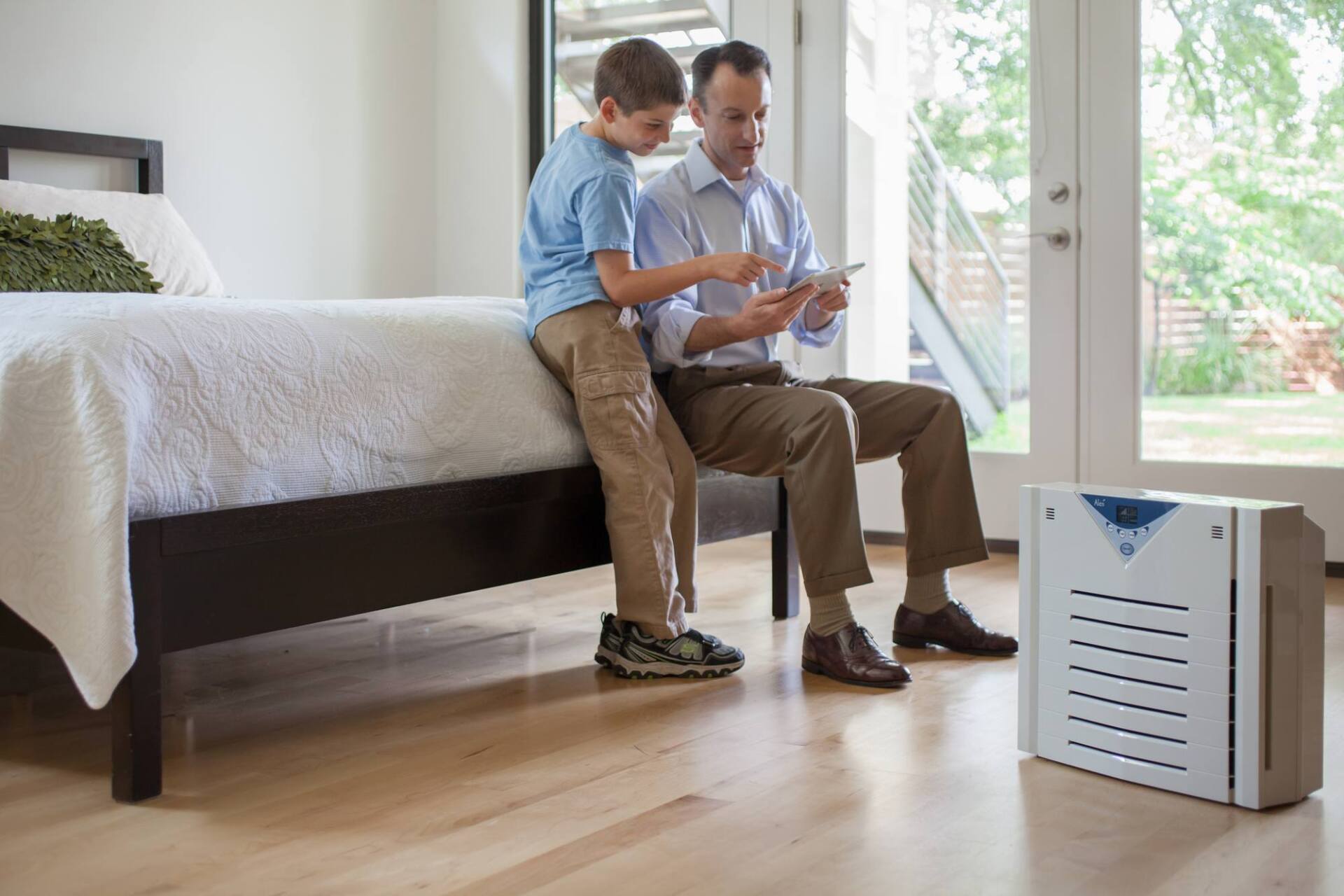 Father and child looking at a tablet together in a bedroom with an air purifier.