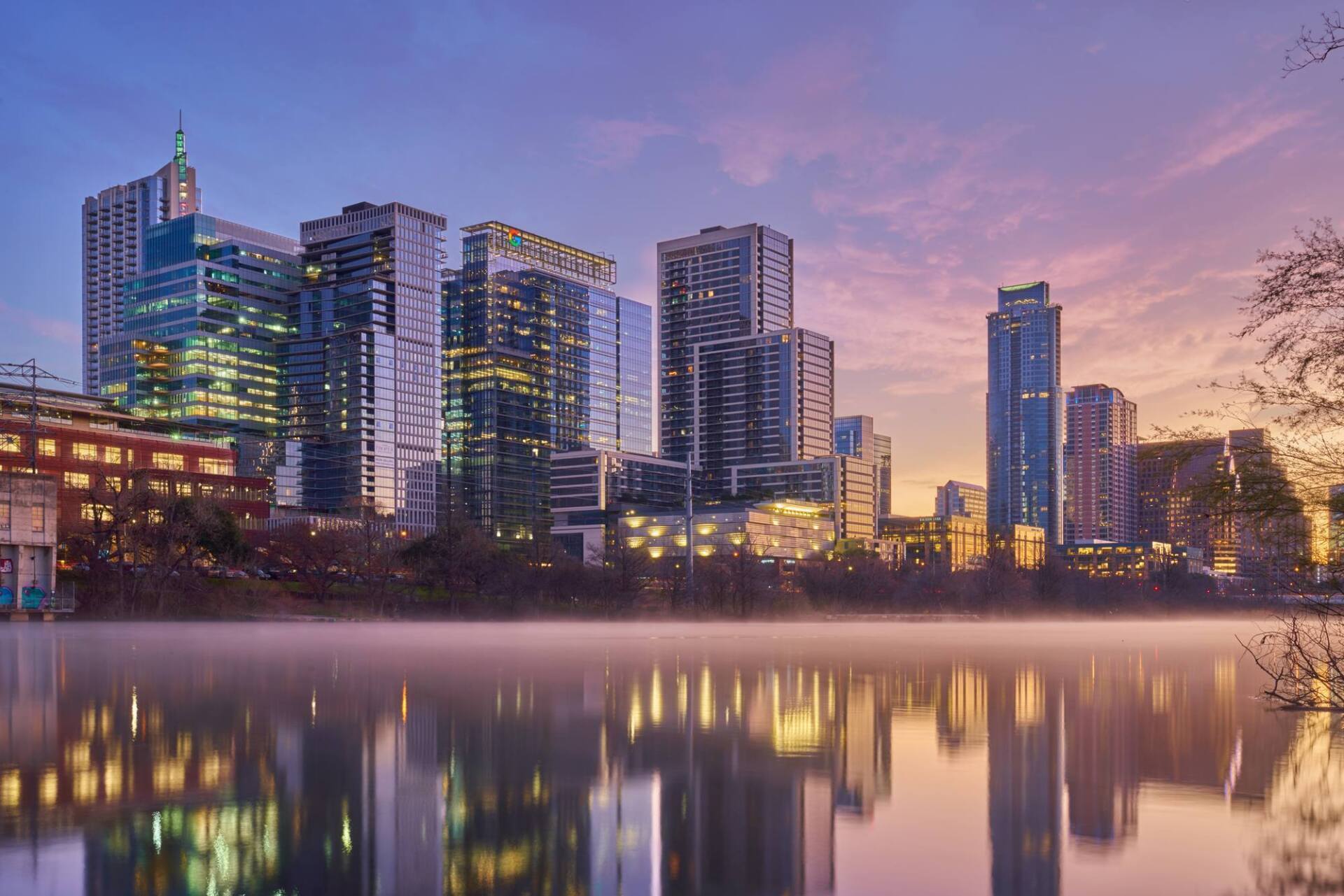 Austin, Texas skyline at dusk reflected in a calm lake with purple and orange sky.