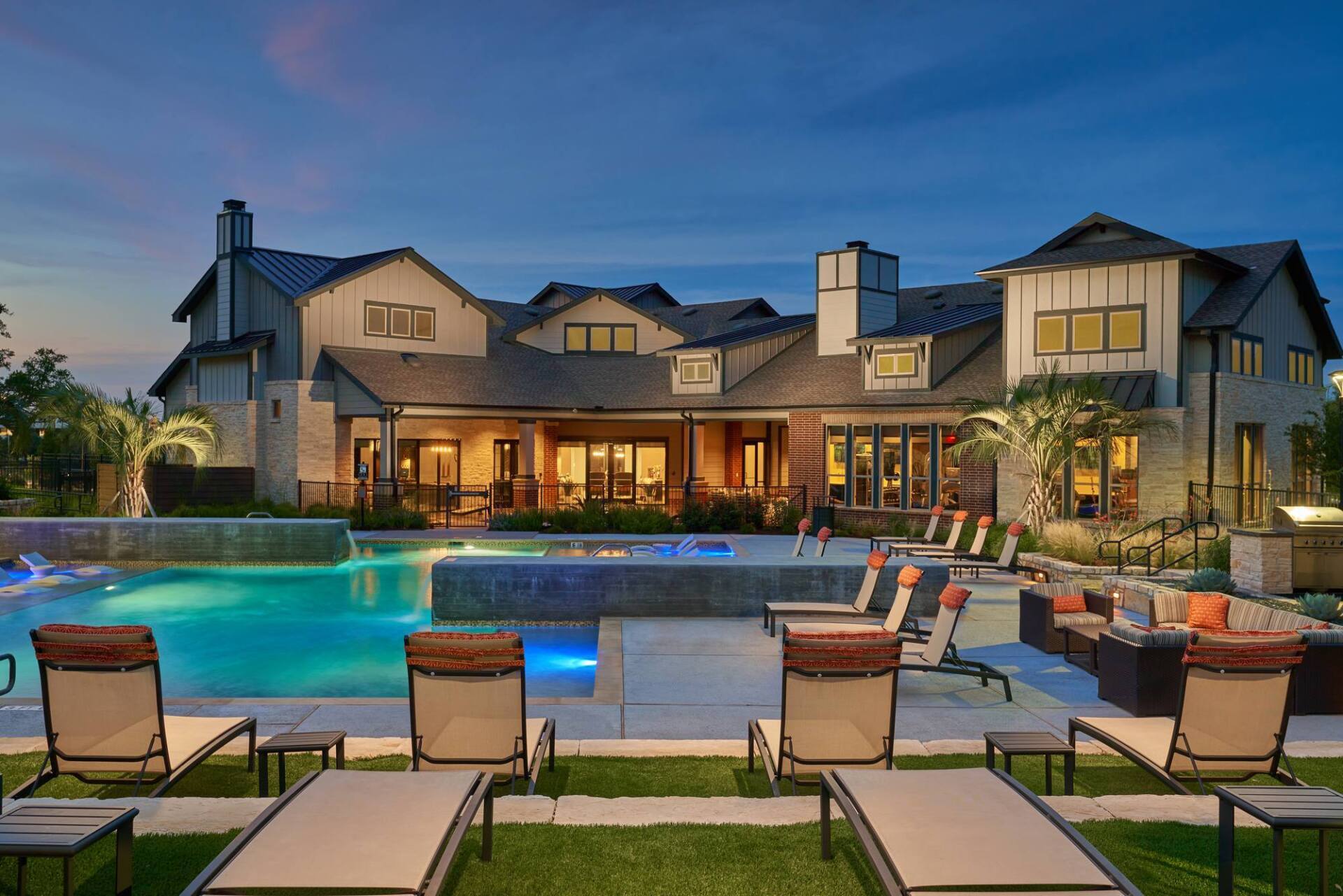 Luxury home at dusk with pool, lounge chairs, and lit patio.