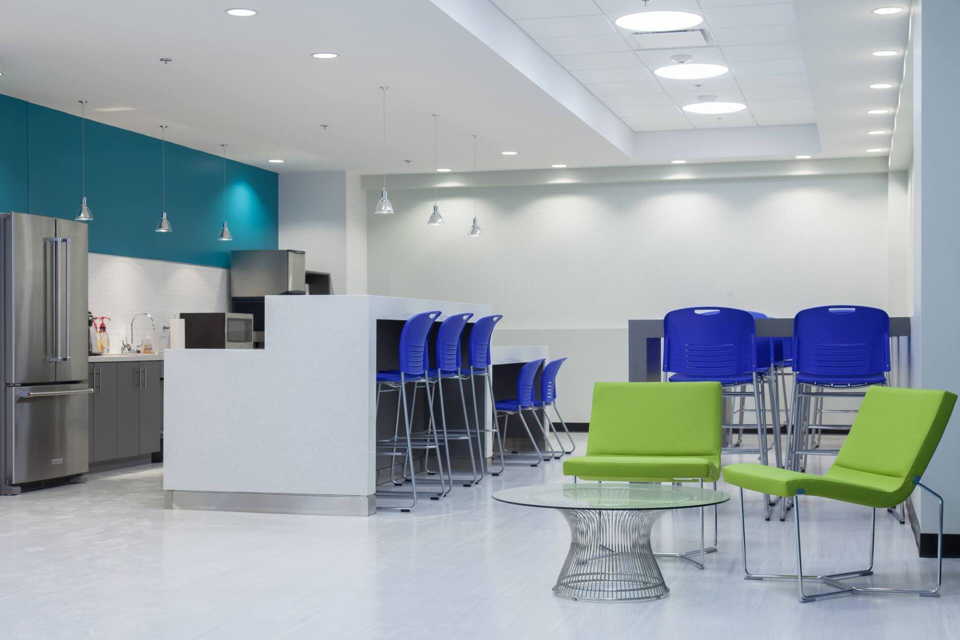 Office break room with turquoise and white walls, stainless steel appliances, and blue and green seating.