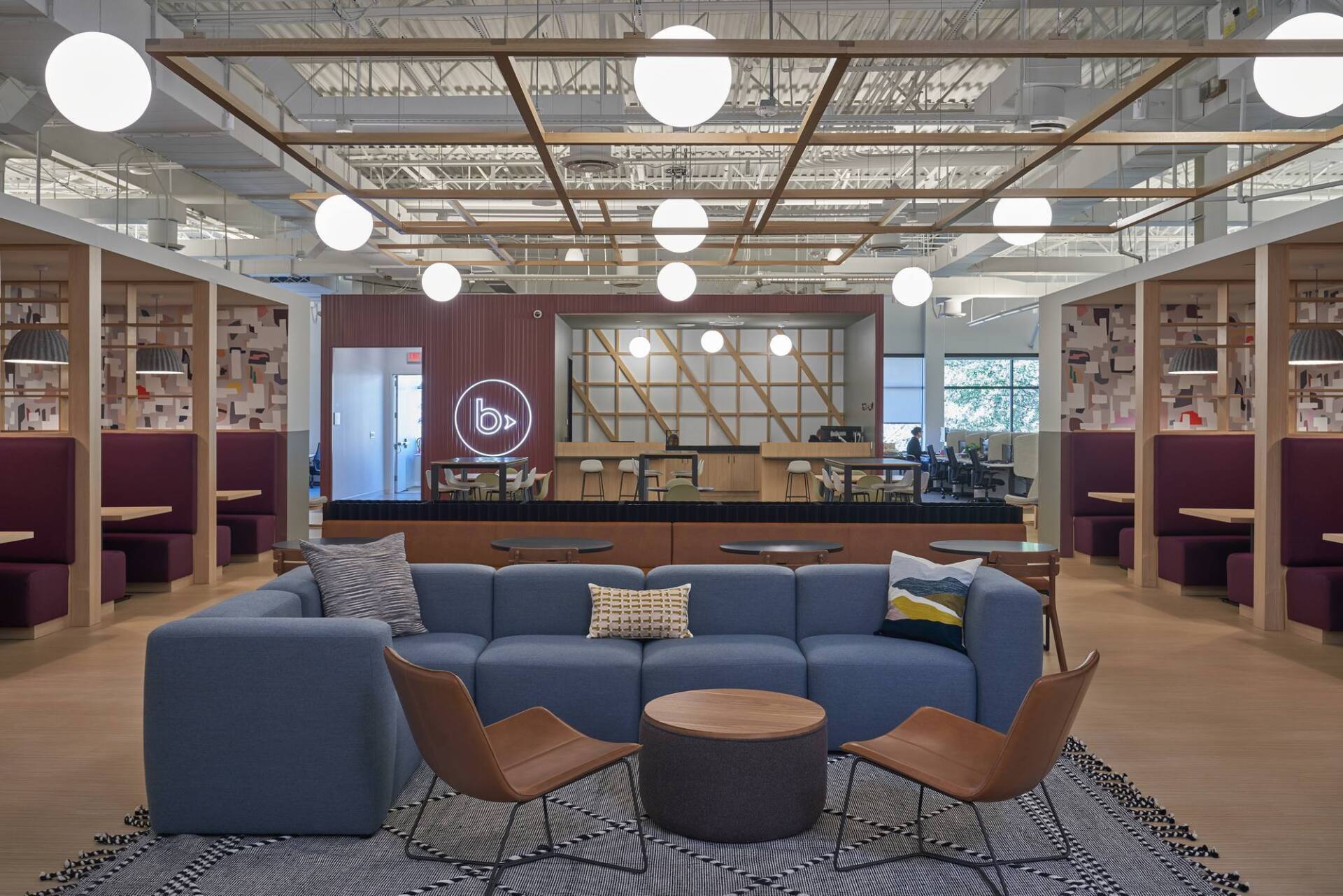 Open office with blue sectional sofa, brown chairs, round table, and multiple work booths.