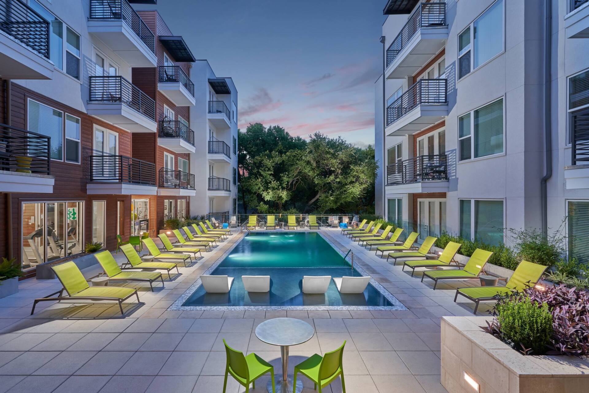 Pool and lounge chairs between two apartment buildings at dusk.