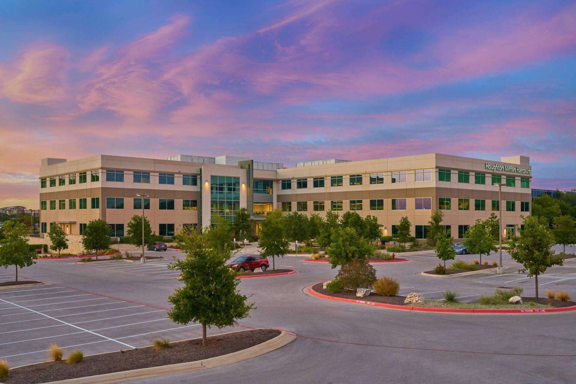 Office building exterior with a colorful sunset sky. Parking lot and trees in the foreground.
