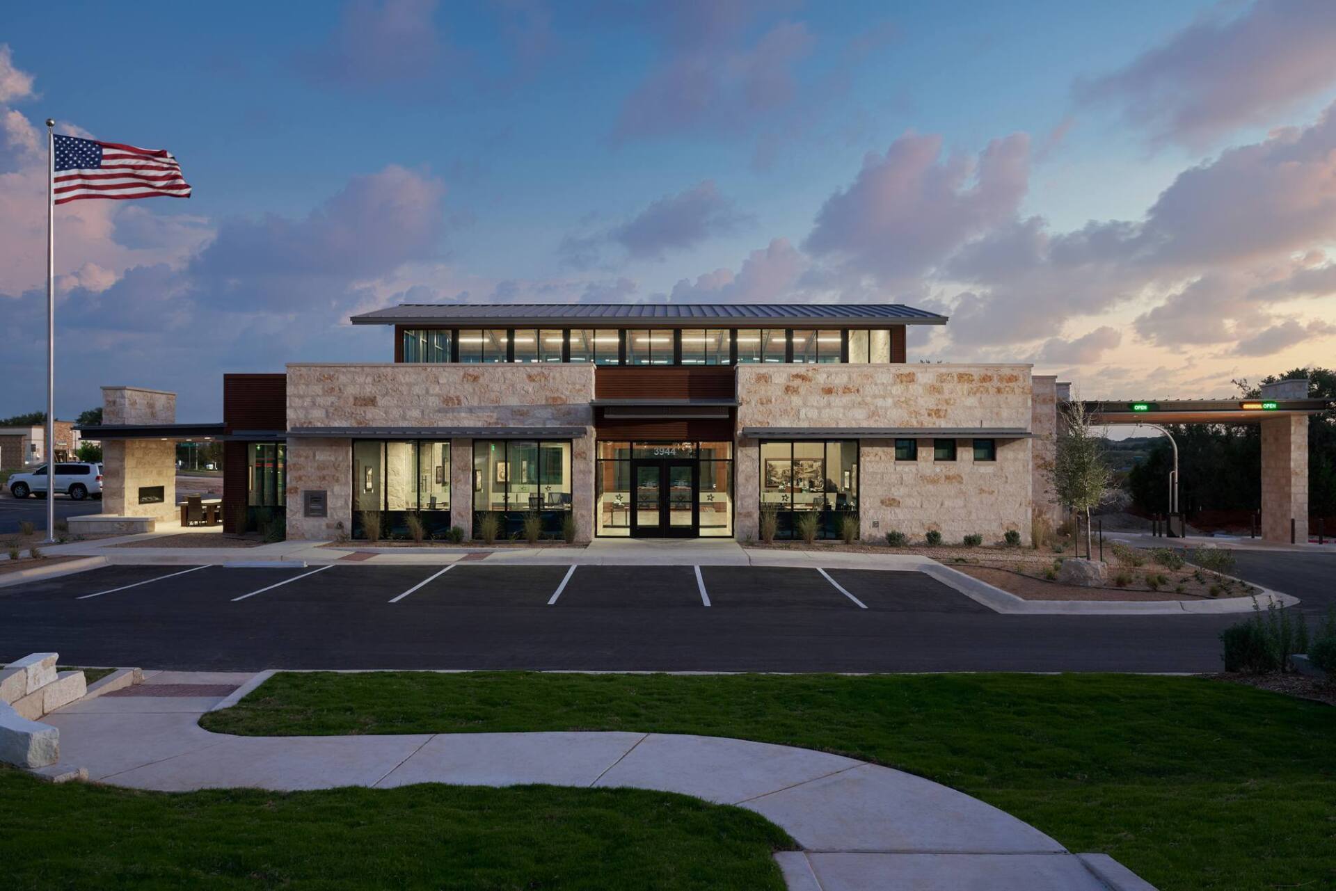 Bank building with stone facade, American flag, and drive-through under evening sky.
