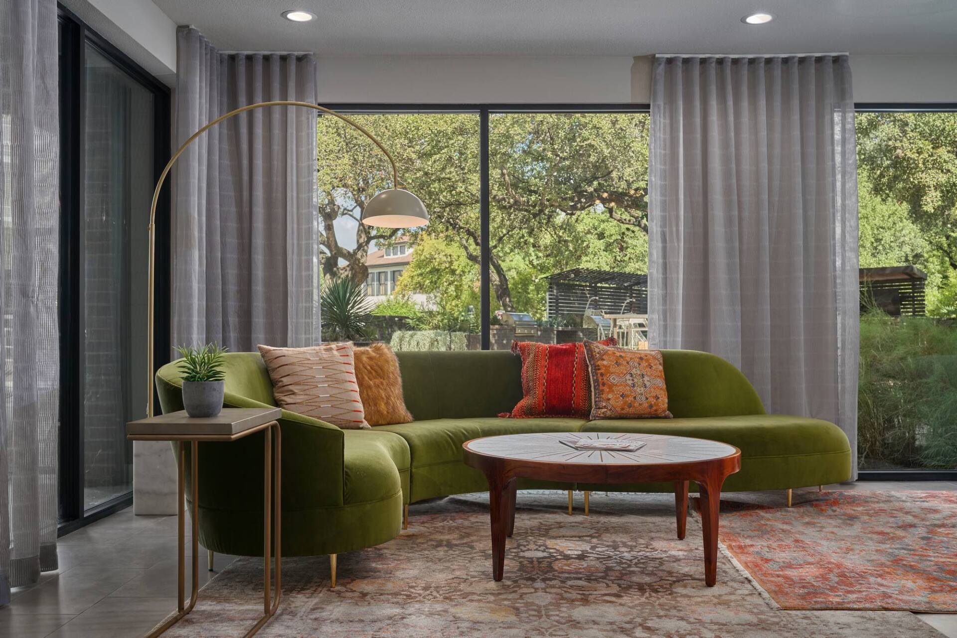 Green sectional sofa in a bright living room with large windows and colorful pillows.