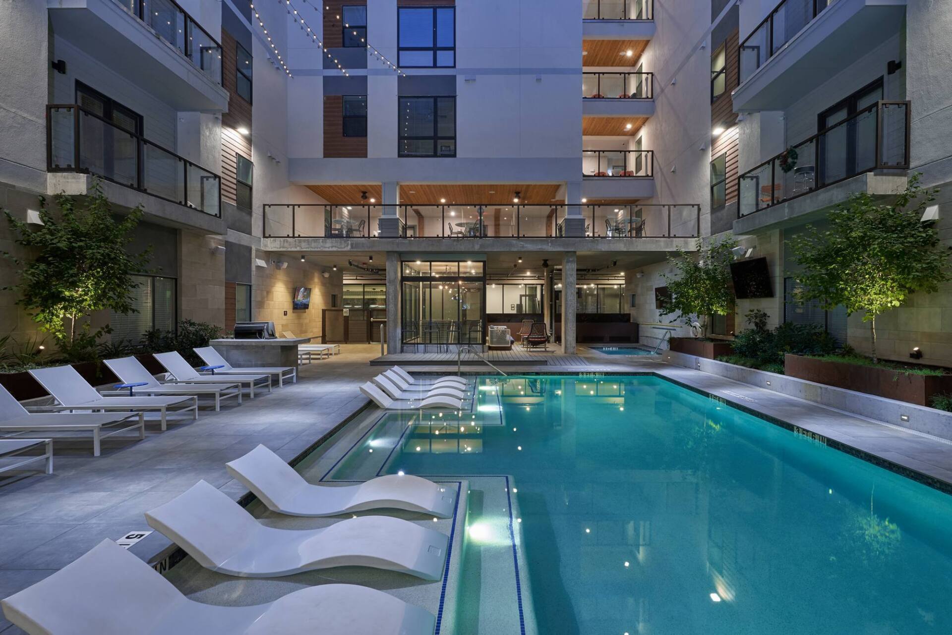Pool area of a modern apartment complex with lounge chairs, blue water, and building balconies.